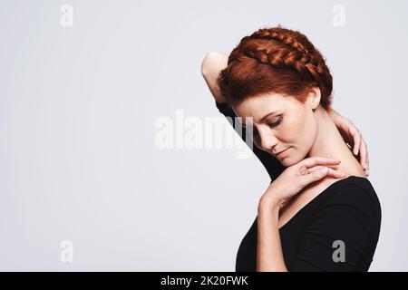 Lassen Sie ihren Hals atmen. Studioaufnahme einer schönen Rothaarigen Frau mit einem geflochtenen Up-Do vor grauem Hintergrund. Stockfoto