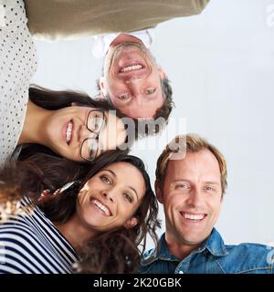 Vertrauen in unsere kollaborative Planung. Aufnahmen aus dem niedrigen Winkel von vier Personen, die die Kamera positiv anlächeln. Stockfoto