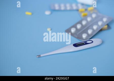 Draufsicht auf Medikamente, Thermometer auf blauem Hintergrund. Er lag flach. Erste-Hilfe-Set - Pillen, Thermometer, Tropfen. Flach liegend. Tablets in einem Stockfoto