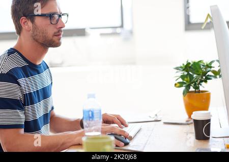 Ein hübscher junger Mann, der im Büro an seinem pc arbeitet. Stockfoto