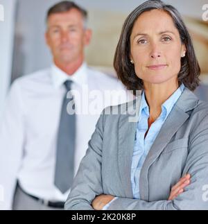 Erfolg und nicht weniger. Porträt einer reifen Geschäftsfrau mit ihrem Kollegen im Hintergrund. Stockfoto