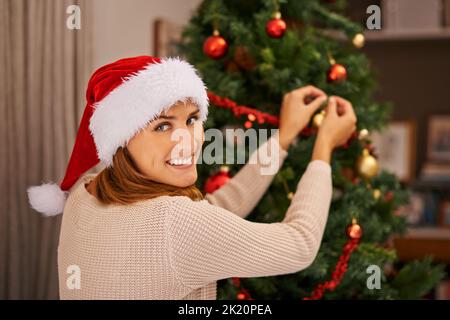 Und so dekorieren Sie den perfekten Baum. Eine schöne junge Frau schmückt ihren Weihnachtsbaum zu Hause. Stockfoto