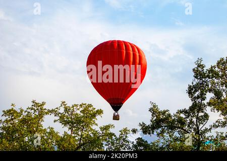 Großer roter Ballon über Berggipfeln am wolkigen Himmel Stockfoto