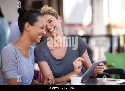 Technologie bringt Menschen näher. Zwei junge Frauen, die in einem Café ein Tablet betrachten. Stockfoto