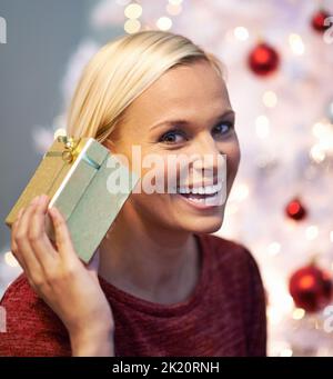 Das Geschenk erraten. Porträt einer attraktiven jungen Frau, die ein Geschenk an ihr Ohr hält. Stockfoto