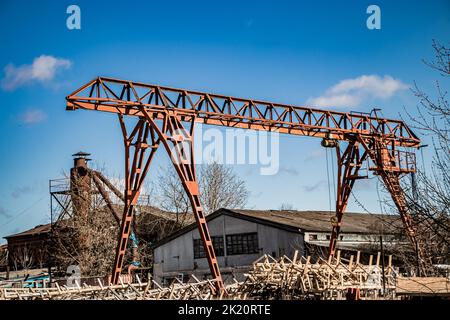 Alter rostiger Portalkran auf verlassene Baustelle. Baumaschinen gegen blauen Himmel. Metallausrüstung in Fabriken, Industrie. Stockfoto