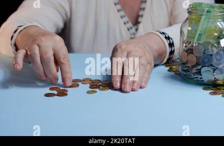 Hände einer älteren Frau mit Geld ron auf der Brieftasche auf blauem Hintergrund. Konzept der Armut im Ruhestand Stockfoto