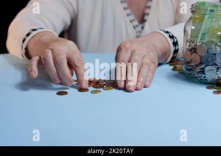 Hände einer älteren Frau mit Geld ron auf der Brieftasche auf blauem Hintergrund. Konzept der Armut im Ruhestand Stockfoto