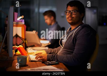 Eine Gruppe junger Mitarbeiter, die in einem schwach beleuchteten Büro arbeiten. Stockfoto