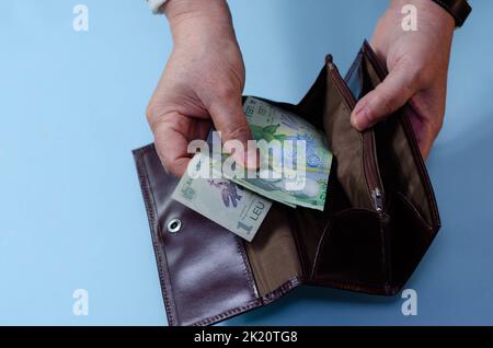 Hände einer älteren Frau mit Geld ron auf der Brieftasche auf blauem Hintergrund. Konzept der Armut im Ruhestand Stockfoto