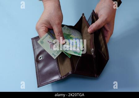 Hände einer älteren Frau mit Geld ron auf der Brieftasche auf blauem Hintergrund. Konzept der Armut im Ruhestand Stockfoto