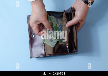 Hände einer älteren Frau mit Geld ron auf der Brieftasche auf blauem Hintergrund. Konzept der Armut im Ruhestand Stockfoto