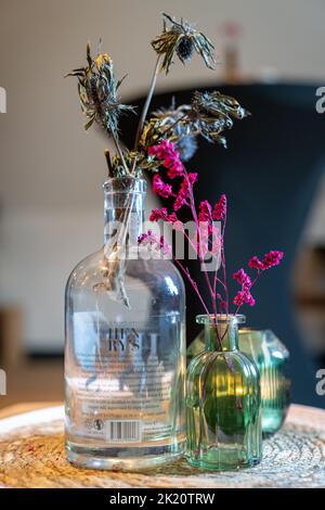 Eine vertikale Aufnahme von bunten Blumen in Vasen auf einem kleinen Holztisch Stockfoto
