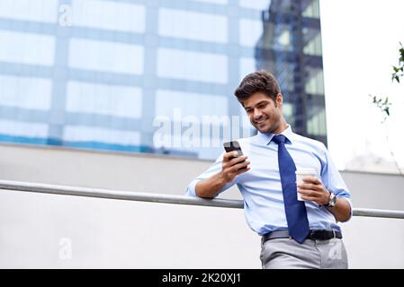 Eine wohlverdiente Pause. Eine Aufnahme eines hübschen jungen Geschäftsmannes, der sein Mobiltelefon in der Stadt benutzt. Stockfoto