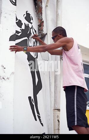 Sich durch Kunst auszudrücken. Ein junger Graffiti-Künstler, der ein Design an eine Wand malt. Stockfoto