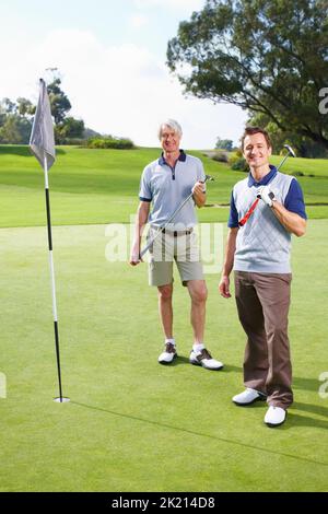 Vater und Sohn Golf spielen. Vater und Sohn stehen auf dem Putting Green mit Golfschlägern und lächeln. Stockfoto
