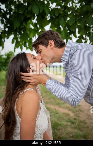 Das Paar inmitten der Natur küsst zärtlich auf den Mund, sie sitzt, er beugte sich um. Stockfoto