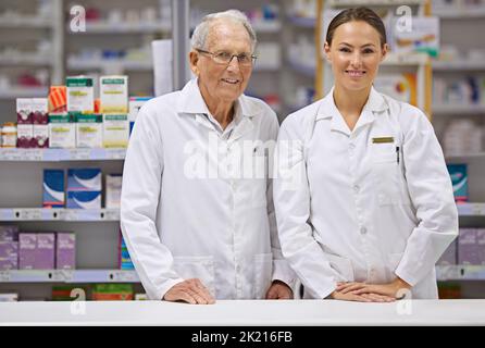 Langjährige pharmazeutische Erfahrung. Ein älterer Apotheker und ein junger Apotheker stehen an der Theke. Stockfoto