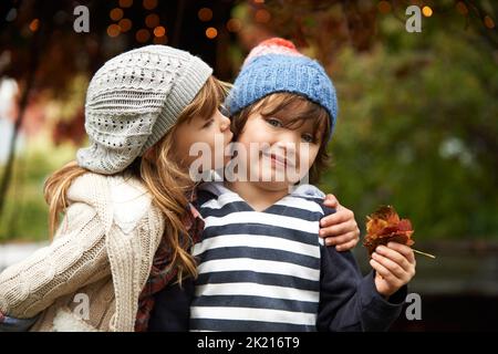 Eeeuwww Brutto. Ein süßer kleiner Junge, der schüchtern aussieht, als seine Schwester seine Wange küsst. Stockfoto