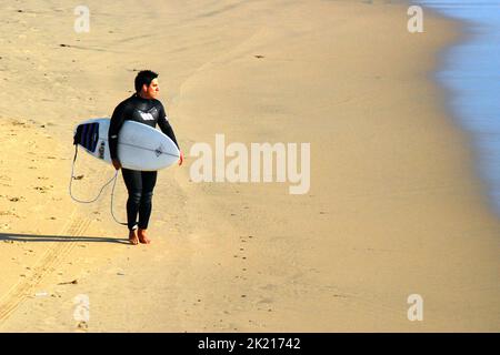 Ein junger Surfer blickt auf den Ozean, während er sich auf das Surfen im Meer vor Huntington Beach in der Nähe von Los Angeles in Südkalifornien vorbereitet Stockfoto