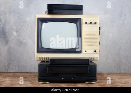 Vintage Retro analoger kleiner Fernseher mit VHS-Video-Player und Videokassetten stehen auf Holzboden vorne grauen Betonwand Hintergrund. Stockfoto