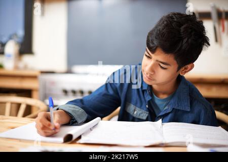 Hes ein fleißiger Schüler. Ein kleiner Junge, der an einem Schreibtisch in einem Klassenzimmer studiert. Stockfoto