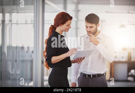 Mit ihrer Strategie immer einen Schritt voraus zu sein. Zwei Kollegen diskutieren im Büro über Papierkram. Stockfoto