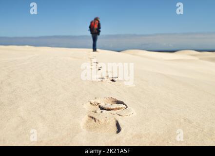 Hinterlässt Spuren. Rückansicht einer jungen Wanderin, die entlang der Sanddünen läuft. Stockfoto