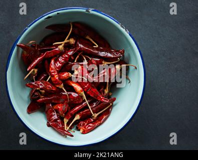 Intensiver Geschmack. In einer Schüssel auf einem Küchentischtisch wurden getrocknete rote Chilischoten aus einem hohen Winkel geschossen. Stockfoto