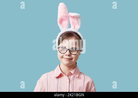Portrait von niedlichen Mädchen mit Down-Syndrom tragen Osterhasen Ohren vor blauem Hintergrund Stockfoto