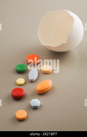 Nahaufnahme der zerrissenen Eierschale, die verschiedene farbige Vitamine und Medikamentenpillen auf hellgrauem Hintergrund enthüllt. Stockfoto