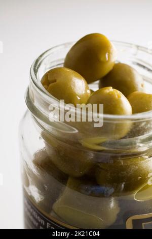 Nahaufnahme grüner gefüllter Oliven im Glasverpackungsglas auf hellgrauem Hintergrund. Stockfoto