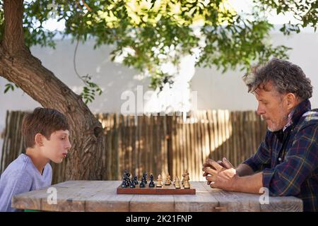 Mit seinem Großvater seine Schachkünste verbessern. Ein kleiner Junge spielt mit seinem Großvater Schach. Stockfoto