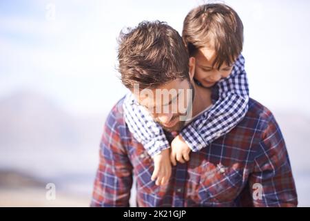 Egal, welcher Vater, du bist mein Held. Ein Vater, der seinen kleinen Sohn auf dem Rücken trägt, während er nach unten blickt. Stockfoto