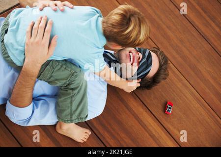 So froh, dass Väter zu Hause sind. Ein kleiner Junge, der mit seinem Vater auf dem Boden spielt. Stockfoto