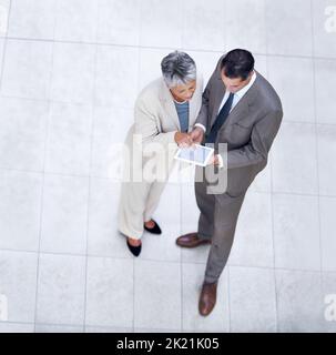 Zwei Köpfe sind besser als einer. Aufnahme von zwei Geschäftskollegen, die mit einem digitalen Tablet stehen und über die Arbeit sprechen. Stockfoto
