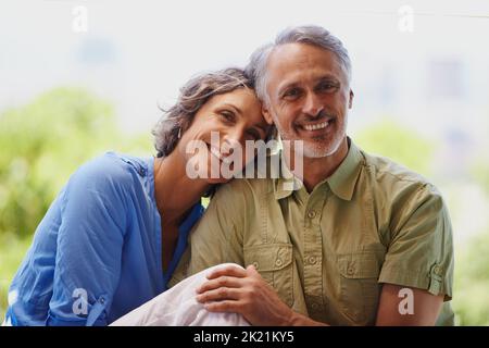 Sie passen perfekt zusammen. Ein beschnittenes Porträt eines glücklichen, mittleren Erwachsenen-Paares, das an einem sonnigen Tag draußen sitzt. Stockfoto