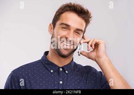 Es ist toll, Ihre Stimme zu hören. Ein hübscher Mann lächelt, während er einen Anruf auf seinem Handy entgegennimmt. Stockfoto