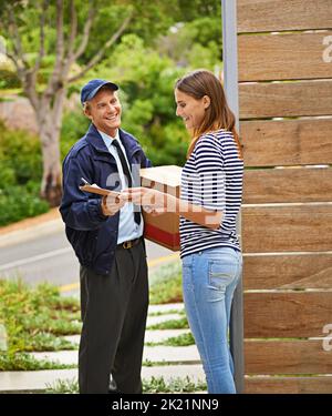 Service mit einem Lächeln. Ein männlicher Kurier liefert ein Paket an eine Frau zu Hause. Stockfoto