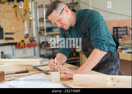 Ein Zimmermann mißt Holzbohlen und macht in einer Werkstatt mit einem Bleistift Markierungen. Stockfoto