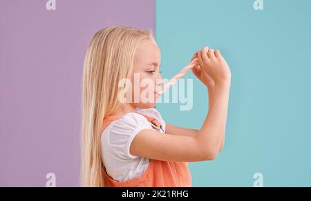 MMM, es ist so zäh. Ein nettes kleines Mädchen, das Süßigkeiten vor einem bunten Hintergrund isst. Stockfoto