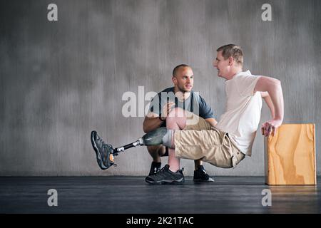 Ein Physiotherapeut hilft einem jungen männlichen Amputierten beim Training. Stockfoto