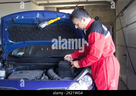 Bild eines Mechanikers in seiner Werkstatt, der eine Autobatterie ersetzt. Wartungsarbeiten Stockfoto