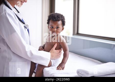 Gerade in für eine routinemäßige pädiatrische Untersuchung. Eine weibliche Kinderärztin, die eine Untersuchung an einem entzückenden kleinen Jungen macht. Stockfoto