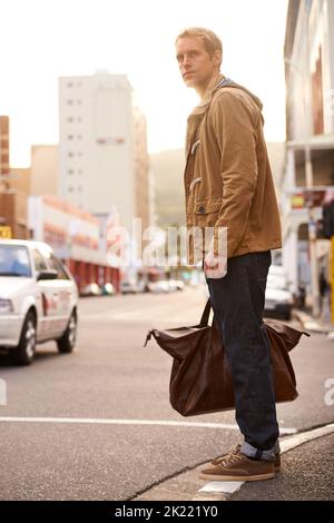 Immer unterwegs. In voller Länge ein modischer Mann, der darauf wartet, eine Straße in der Stadt zu überqueren. Stockfoto