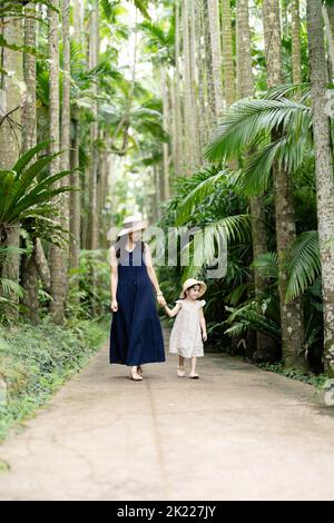 Mutter und Tochter wandern zwischen den tropischen Palmen des Southeast Botanical Gardens in Okinawa, Japan Stockfoto