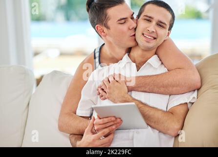 Wir hätten uns nicht mehr verliebt. Porträt eines liebevollen schwulen Paares, das ein digitales Tablet benutzt, während es sich zu Hause auf dem Sofa entspannt. Stockfoto