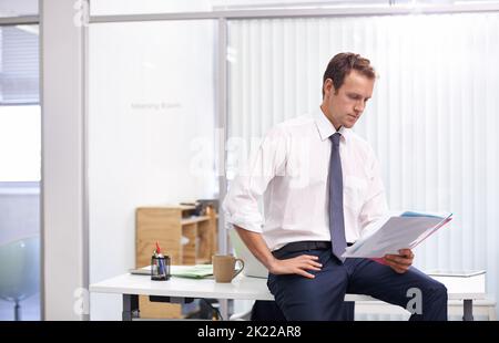 Der Fokus liegt auf den Finanzen. Ein hübscher junger Geschäftsmann liest in seinem Büro Dokumente durch. Stockfoto