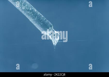 Ein Tropfen feuchtigkeitsspendendes Serum aus einer Pipette. Auf blauem Hintergrund. Stockfoto