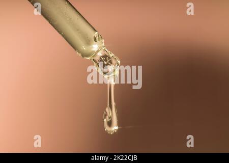 Ein Tropfen feuchtigkeitsspendendes Serum aus einer Pipette. Auf einem orangefarbenen Pfirsich-Hintergrund. Stockfoto